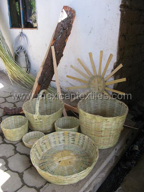 canastas_ixtolco_19.JPG - In this photo we can see all the material and process steps. The background has the split bamboo, the wood trunk is finely split leaning against the log is a piece of pine split from the log , which is used to form the basket. The star like piece is the beginings of the baskets, basicly its foundation. In the forground we can see a number of different products.